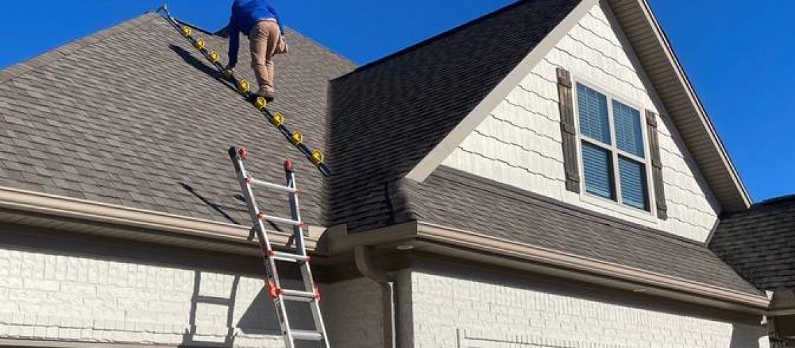 Worker on a ladder inspecting the shingle roof of a two-story house